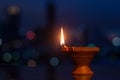 Selective focus on flame of clay diya lamp with colorful city bokeh lights.