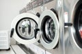 Selective focus on the front door of the washing machine with blurred close doors in foreground. Row of washing machines in the