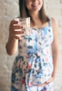 Selective focus of glass of water in hands of pregnant woman