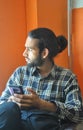 Selective focus of a good looking bearded man with hair bun, looking sideways during using his phone while sitting indoors Royalty Free Stock Photo