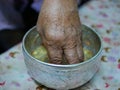 A hand of elderly person dipping into a cup salung filled with holy turmeric water