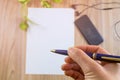 Selective focus, Hand holding a pen write on white paper and modern smartphone on wooden table top view with copy space,blurred Royalty Free Stock Photo