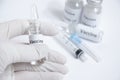 Selective focus on hand in white medical glove holding vaccine vial on blurred background of syringe and ampoule with vaccine. Royalty Free Stock Photo