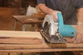 Selective focus on hands of senior carpenter cutting a piece of wood with electric circular saw in carpentry workshop