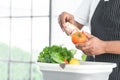 Selective focus on hands of senior man washing tomato and corn at home. Vegetables, lettuce and lemon soak with water in basin.