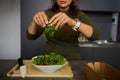 Close-up hands of a woman holding fresh leaves of arugula greens, adding it into a bowl with healthy raw vegan salad Royalty Free Stock Photo