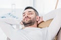 Selective focus of handsome bearded man with eyes closed and Hands Behind Back resting on couch at home. Royalty Free Stock Photo