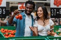 Focus of happy african american man holding tomatoes near asian woman with notebook