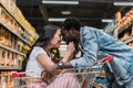 Focus of happy asian girl sitting in shopping cart and touching face of handsome and cheerful african american man Royalty Free Stock Photo