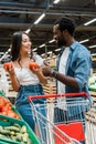 Focus of happy asian woman holding fresh tomatoes near cheerful african american man showing thumb up in supermarket Royalty Free Stock Photo