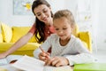 Focus of happy kid studying near babysitter at home