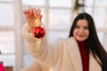 Selective focus of happy smiling woman in fur coat holding red ball for decoration Christmas tree in light room. Closeup Royalty Free Stock Photo