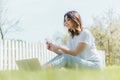 Focus of happy woman using smartphone near laptop while sitting on grass Royalty Free Stock Photo