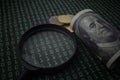 Selective focus image of magnifying glass bank note and coin on a binary code background. Economy and IT concept