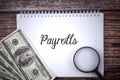 Selective focus image of magnifying glass and bank note with payrolls wording on a wooden background Royalty Free Stock Photo