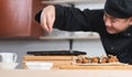 Selective focus on japanese food called takoyaki in plate from hot pan on table. Asian young chef man, in black uniform, cooking Royalty Free Stock Photo
