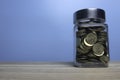 Selective focus jar full with gold coins and copy space on wooden table with a blue background Royalty Free Stock Photo