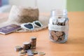 Selective focus at jar glass. Glass full of money coin with blurred straw hat, sunglasses and passport mock up at the background. Royalty Free Stock Photo