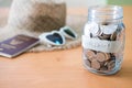 Selective focus at jar glass. Glass full of money coin with blurred straw hat, sunglasses and passport mock up at the background. Royalty Free Stock Photo