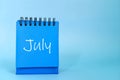 Selective focus of July month desk calendar on blue background with copy space.