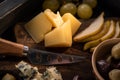 Selective focus of knife, pieces of cheese, slices of pear, dried olives, grapes on cutting board on tray.