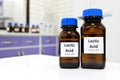 Selective focus of lactic acid liquid solution in dark brown glass bottle in a white chemistry laboratory background. Chemical