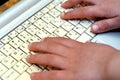 a laptop keyboard with English and Arabic Alphabet with an out of focus child's hand typing on a white keyboard Royalty Free Stock Photo