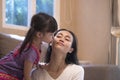 Little Asian girl kissing her mother`s cheek in living room at home Royalty Free Stock Photo