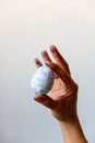 selective focus male hand stained with blue paint holding a freshly painted Easter egg against a white wall