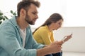 Focus of man using smartphone near girlfriend chatting in living room