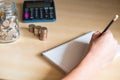 Selective focus at men hand while writing personal saving plan on the paper with blurred stack of money coins, glass jar coin and Royalty Free Stock Photo