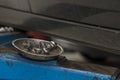 Selective focus. Metal bowl with bolds from a car wheel next to the side of a black car in a garage workshop