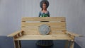 Miniature toy doll women in dress with hat and handicrafts bench chair