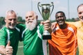 selective focus of multiethnic smiling old sportsmen with champions cup standing
