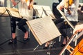 Selective Focus on Music note sheets on stand with background of playing cellists and violinists band on event in bright day sunli Royalty Free Stock Photo
