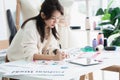 Selective focus on newspaper placed on desk of Asian beautiful woman fashion designer or dressmaker drawing sketch of new Royalty Free Stock Photo