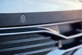 Selective focus on parking sensor of parking assistent system at front of luxurious car bumper close up on light blurred Royalty Free Stock Photo