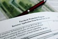 Selective focus photo of paycheck protection program borrower application form revised, on a background of dollar bills and a pen