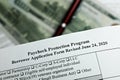 Selective focus photo of paycheck protection program borrower application form revised, on a background of dollar bills and a pen