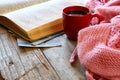 Selective focus photo of pink cozy knitted scarf with to cup of coffee, wool yarn balls and open book on a wooden table