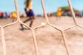 Selective focus photo of an unrecognizable player running with a ball near the goal during a soccer game on a beach in