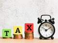 Selective focus phrase TAX on colorful wooden cubes with alarm clock and coins. Royalty Free Stock Photo