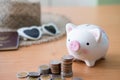 Selective focus at piggy bank. Stack of money coin with blurred straw hat, sunglasses and passport mock up at the background. Royalty Free Stock Photo