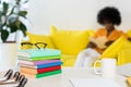 selective focus of pile of books, eyeglasses, cup of coffee at workplace and african american freelancer on sofa on background