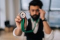 Selective focus portrait of blurred Indian male doctor in glasses holding stethoscope on hand for listening check up Royalty Free Stock Photo