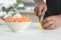 Selective focus at radish on sliced fresh salmon sashimi on bowl with ice. Asian senior man`s hand holding knife slicing lemon Royalty Free Stock Photo