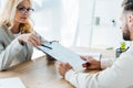 Focus of recruiter holding clipboard and pen and sitting near employee