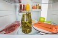 Selective focus of sausages with chili peppers and pickles in fridge with open door Royalty Free Stock Photo