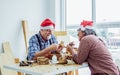 Selective focus senior Caucasian retired old man wearing santa hat, check shirt with apron, painting wooden figure as hobby after