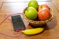 Selective focus shot of apples in a braided bowl, a banana, a phone with earphones on the table
